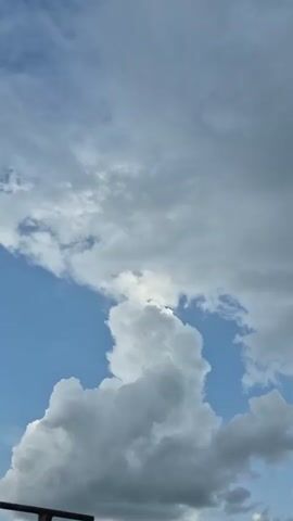 The video displays a time-lapse of clouds moving across a blue sky. The clouds are a mix of gray and white, indicating a potentially overcast or changing weather condition. The camera angle is looking upwards, focusing solely on the sky. No people, objects, or specific locations are visible. The movement of the clouds is gradual, suggesting the passage of time.