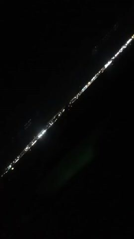 The video shows a string of lights, presumably from a city, viewed through a car window at night. The lights form a diagonal line across the frame, with the rest of the scene being mostly black. A brief glimpse of red is visible at one point, likely from inside the car.