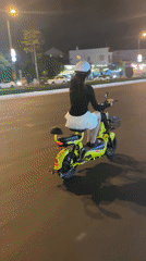 Woman rides yellow scooter through nighttime Phan Thiết streets
