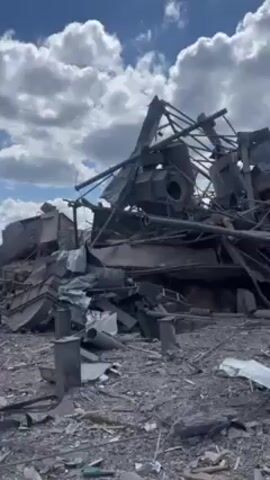 Here is a concise description of the video:

The video shows the aftermath of a destructive event, possibly an explosion or targeted demolition, leaving a scene of twisted and mangled metal debris scattered across the ground. The remnants of what was likely a substantial structure are visible in the foreground, revealing bent support beams, fragmented metal sheets, and unidentified machinery parts. The sky above is bright, featuring scattered clouds, adding a stark contrast to the devastation below. The overall atmosphere conveys a sense of ruin and destruction, with no signs of activity or presence of people in the immediate view.