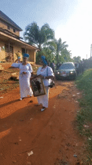 Women in ceremonial dress gather on dirt road in Obosi