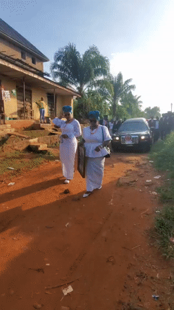 Women in ceremonial dress gather on dirt road in Obosi