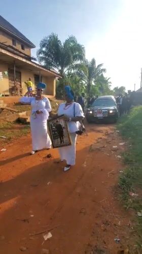 Women in ceremonial dress gather on dirt road in Obosi