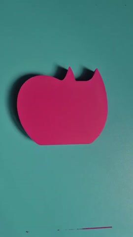 The video shows a pink cat-shaped sticky note on a teal surface. The sticky note is casting a shadow. A faint pink line is visible at the bottom of the screen.