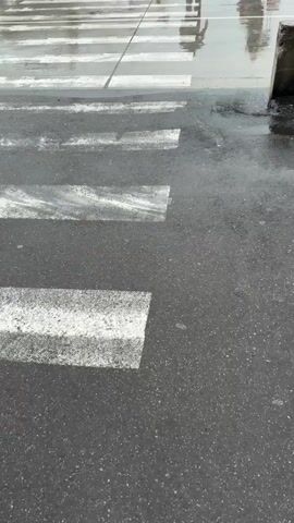 The video shows passengers disembarking from a white and pink Wizz Air plane with the word "KUTAISI" printed on it, on a rainy day at an airport. People are walking across the wet tarmac toward the camera, some pulling luggage. The airplane is connected to a set of stairs with a vehicle at the base, also labeled "KUTAISI." Ground crew are seen near the plane. The overall scene suggests a recent arrival or departure on a wet day.