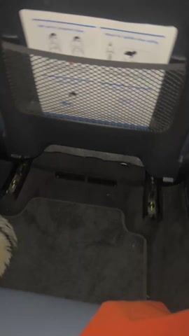 The video shows the interior of a vehicle at night. The camera is positioned in the back seat, looking forward. The rear center console has a screen displaying a navigation map. The console has a logo on it that appears to be a "W." In the front, the car's dashboard with multiple digital screens is visible. The car is moving through a city at night. Traffic lights are visible outside the window. A person wearing orange pants and furry sandals is sitting in the back seat.