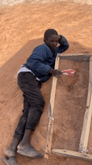 Boy sifts dirt through mesh frame in Nigeria village