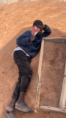 Boy sifts dirt through mesh frame in Nigeria village