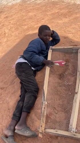 Boy sifts dirt through mesh frame in Nigeria village