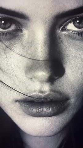This is a close-up, black and white video of a person's face, focusing on the eyes, nose, and lips. A strand of hair is visible across the face, obscuring part of the nose. The lighting appears dramatic, creating shadows that highlight the contours of the face. The texture of the skin is visible, with some fine lines and subtle imperfections. The overall mood is intense and somewhat melancholic due to the lighting and expression.