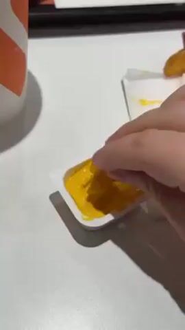 A person dips a potato wedge into a small container of yellow sauce. The camera pans back to show a fast food tray with two containers of yellow sauce, two orange and white cups, and two orange containers of fries. The person eats a fry.