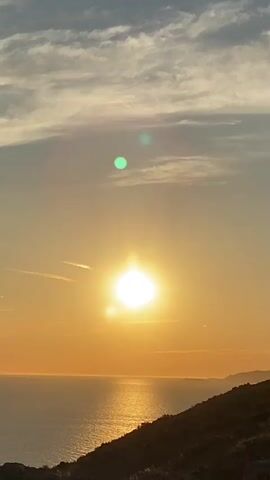 The video shows a view of the ocean at sunset. The sun is low in the sky, casting a warm glow over the water. The sky is filled with wispy clouds, and the overall scene is peaceful and serene.