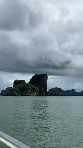 A boat is moving through the water towards a cluster of islands. The islands are rocky and covered in green vegetation. The sky is cloudy and gray.