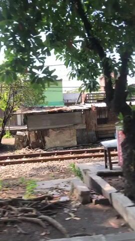 The video shows a street scene with a truck. The truck is green and yellow and appears to be carrying some sort of cargo. There are some people near the truck, possibly unloading or loading it. The area around the truck appears to be somewhat cluttered, with debris and construction materials visible. In the background, there are buildings and trees, and the sky is visible. There are also power lines running overhead. The scene appears to be in an urban or semi-urban environment.