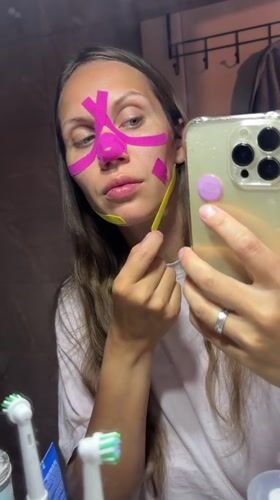 Woman applies kinesiology tape to face in Fethiye bathroom