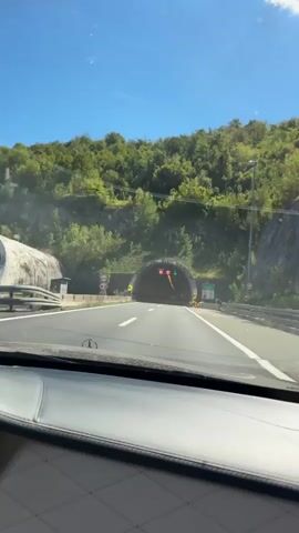 The video shows a first-person perspective of driving through a tunnel. The entrance to the tunnel is visible with overhead lights and signs. As the car enters the tunnel, the lighting changes to a warm yellow, illuminating the concrete walls and ceiling. The road ahead is clearly marked with lane lines. The video continues as the car progresses through the tunnel, with the perspective remaining focused on the road and the tunnel's interior. The scene is devoid of other vehicles or individuals within the immediate view. The ambient sound is consistent with driving.