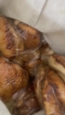 The video shows a close-up view of food items wrapped in plastic. The food appears to be baked or fried, with a golden-brown color. The items are irregular in shape and seem to be small pieces. The plastic wrap is transparent and slightly crinkled. The background is blurred, but it appears to be a light-colored surface. The next clip shows the food items now in a bright green bowl, unwrapped. They are pieces of food that are golden brown and have a slightly irregular, flattened shape. The bowl is a bright green plastic.
