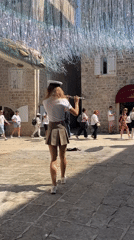 Woman plays flute in sunlit Budva square