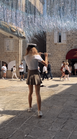 Woman plays flute in sunlit Budva square