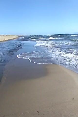 The video shows a beach with waves lapping at the shore. The sand is wet and appears to be a light brown color. The ocean is a deep blue with whitecaps on the waves. The sky is clear and blue. There are no people or objects visible in the video. The video appears to be a static shot with no movement.
