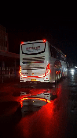 Illuminated rainbow-design bus parked on wet Lhokseumawe street