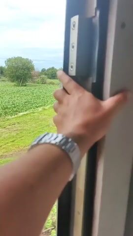 A hand wearing a silver watch opens a train door, revealing a view of lush green fields and trees under a cloudy sky. The hand reaches out, and the door swings open, showing a glimpse of the passing landscape. The video captures the motion of the door and the scenery outside.