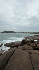 Woman sits on rocky Sri Lankan coastline during overcast morning