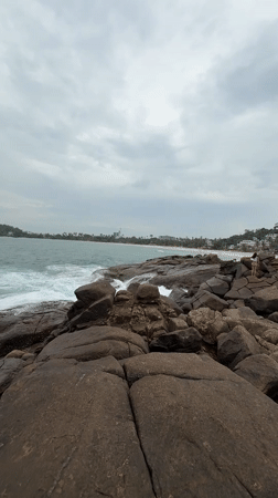 Woman sits on rocky Sri Lankan coastline during overcast morning