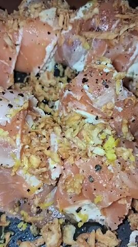 Here is a description of the video:
The video shows a close-up of a plate of appetizers. The appetizers consist of slices of salmon layered with a white creamy substance and topped with fried onions. The plate is black and round. To the side of the plate, there is a glass of water. The camera zooms out slowly to show the whole plate.