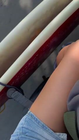 The video shows a first-person perspective of a person sitting on a vehicle, possibly a bicycle or scooter, with surfboards strapped to it. The camera angle is low, focusing on the person's legs and the surfboards. The surfboards are stacked, with one on top of the other. The person is wearing denim shorts and a sandal. The surfboards appear to be of different colors, one is off-white and the other has a red stripe. There are fins attached to the surfboards, and they are secured with straps and bungee cords. The background is blurred, suggesting movement. The scene appears to be outdoors, possibly on a sunny day, as indicated by the lighting.
