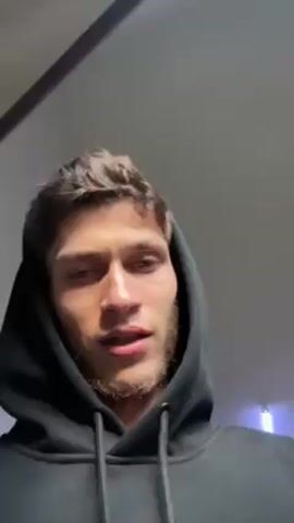 A man with short brown hair and a light beard is looking down at the camera. He is wearing a black hoodie. The ceiling is visible behind him. He says "Guys. Good morning guys."