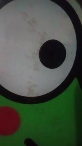 The video shows a close-up of a cartoonish face with a large white eye, a black pupil, a green head, and a red cheek. The image is slightly out of focus and appears to be a still frame from a video, as indicated by the timestamp. There are faint, scratch-like marks visible within the white part of the eye.
