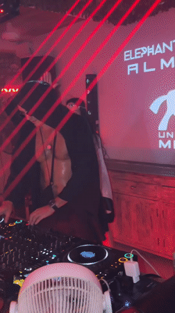 Hooded DJ works a lively booth under colored stage lights