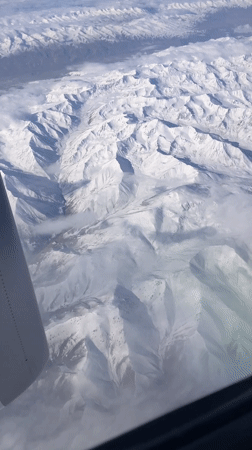 Passenger films snowy mountains, town from airplane near Shymkent