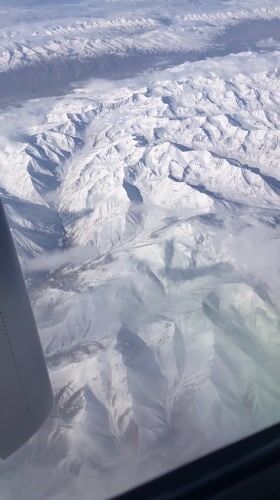 Passenger films snowy mountains, town from airplane near Shymkent