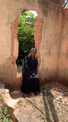 Woman in traditional dress sits in deteriorated building in Jos