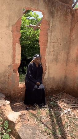 Woman in traditional dress sits in deteriorated building in Jos