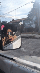 Person films self in vehicle mirror during daytime drive