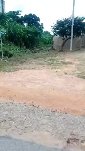 A vehicle is traveling down a dirt road. On the side of the road is dense green vegetation, partially obscuring a grey water tower. The sky is overcast. The camera seems to be handheld, and is shaky. The sound of a vehicle engine can be heard.