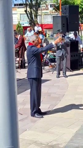 Here is a brief description of the video:

The video shows a wedding celebration taking place outdoors. In the first scene, an older man in a suit is standing and making a toast with a glass of champagne. The scene shifts to show a group of people, including several couples dressed in white or suits, raising their glasses in celebration. Many attendees are taking photos or videos of the couples. The setting appears to be a public park or plaza, with trees and buildings in the background. The atmosphere is festive and celebratory.