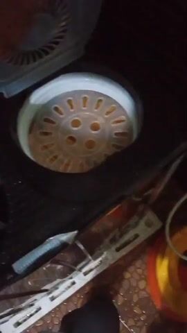 A hand is reaching into a laundry basket and pulling out a bundle of brown clothing. The laundry basket appears to be inside a washing machine. The floor is tiled and there are some cleaning supplies in the background. The lighting is dim.