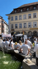 White-shirted crowd gathers in Würzburg square, banner suggests memorial event