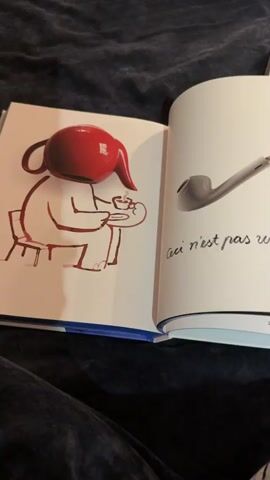 A person's hands are holding open a book with a dark blue blanket in the background. The book has several pages with illustrations and text. The first page shows a drawing of a character with a red teapot for a head sitting at a table with a cup. The page opposite has a drawing of a pipe and some text in French. The next spread shows an illustration of a person in a chair on the left and text on the right. The third spread shows a drawing of a person with yellow legs and a white skirt on the left and text on the right. The final spread shows a drawing of a hedgehog on the left and a person eating something on the right. The video rapidly flips through these pages.