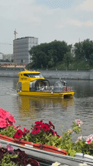 Yellow tourist boat cruises Moscow river past flower-lined embankment