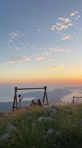 Three people gather at mountain swing set during Montenegro sunset