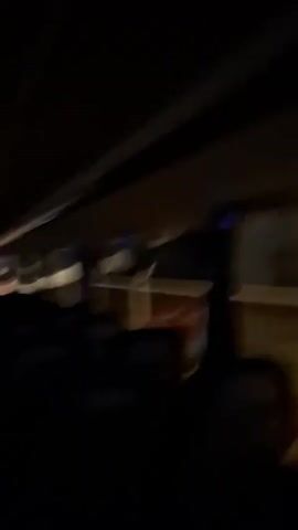 The video shows the interior of a vehicle at night. The perspective is from a passenger seat, looking towards the front. The dashboard is visible, along with the driver's silhouette. The exterior is blurred due to movement, with headlights of other vehicles or streetlights appearing as streaks of light. Audio suggests a person singing.