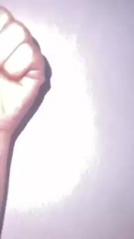 A hand forms a fist against a plain, light-colored wall.  The fist opens up to show a thumb up, then two fingers are extended and then three.