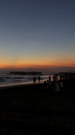 Sunset draws beachgoers to black sand shores in North Kuta