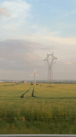 Train passenger captures rural Bulgarian landscape with wind turbine