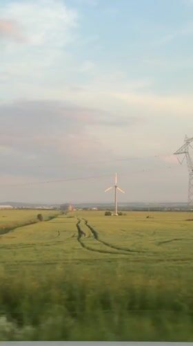 Train passenger captures rural Bulgarian landscape with wind turbine